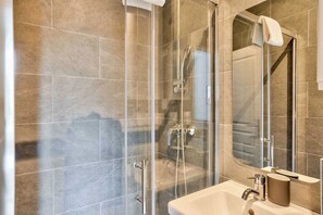Un baño moderno con ducha de vidrio, lavamanos blanco y un espejo grande.