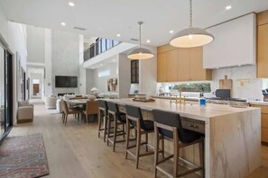 Een moderne keuken met een groot eiland, barkrukken en hanglampen.
