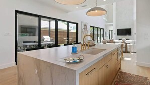 A modern kitchen with a large island, pendant lighting, and a view of the outdoors. - Lux 4100sqft Estate•Rooftop•Pool/Spa (Dallas)