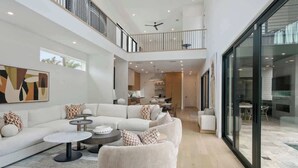 A modern interior with a sectional sofa, round coffee table, and a glass door leading to an outdoor area. - Lux 4100sqft Estate•Rooftop•Pool/Spa (Dallas)