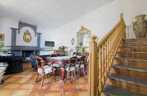 A dining area with a round table and chairs, a fireplace, and a staircase with a wooden railing.