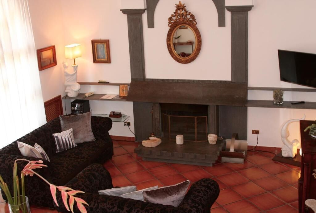 A living room with a fireplace, dark patterned sofa, and a flat-screen TV.