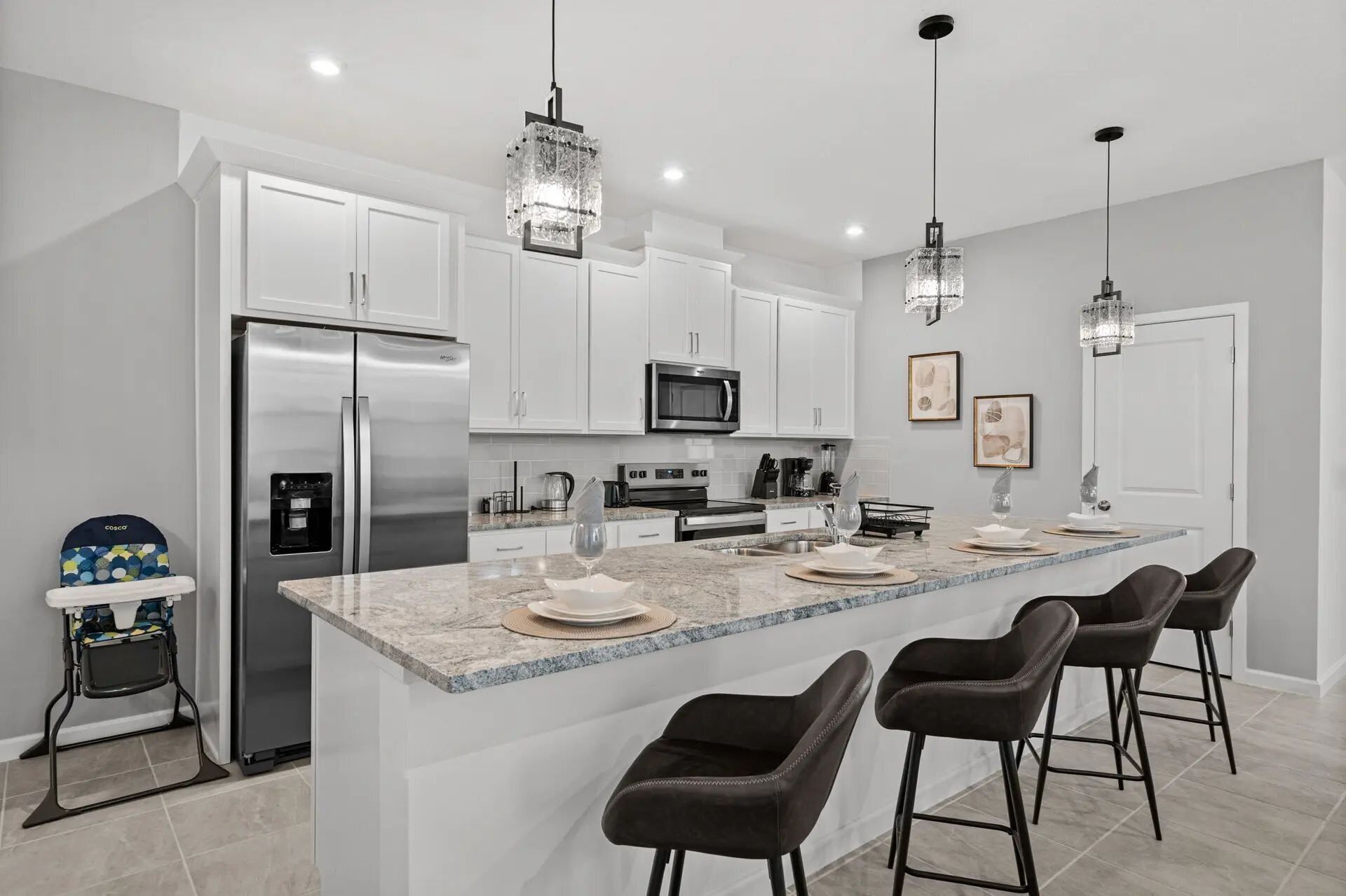 A modern kitchen with white cabinets, stainless steel appliances, a marble island with bar stools, and pendant lighting.