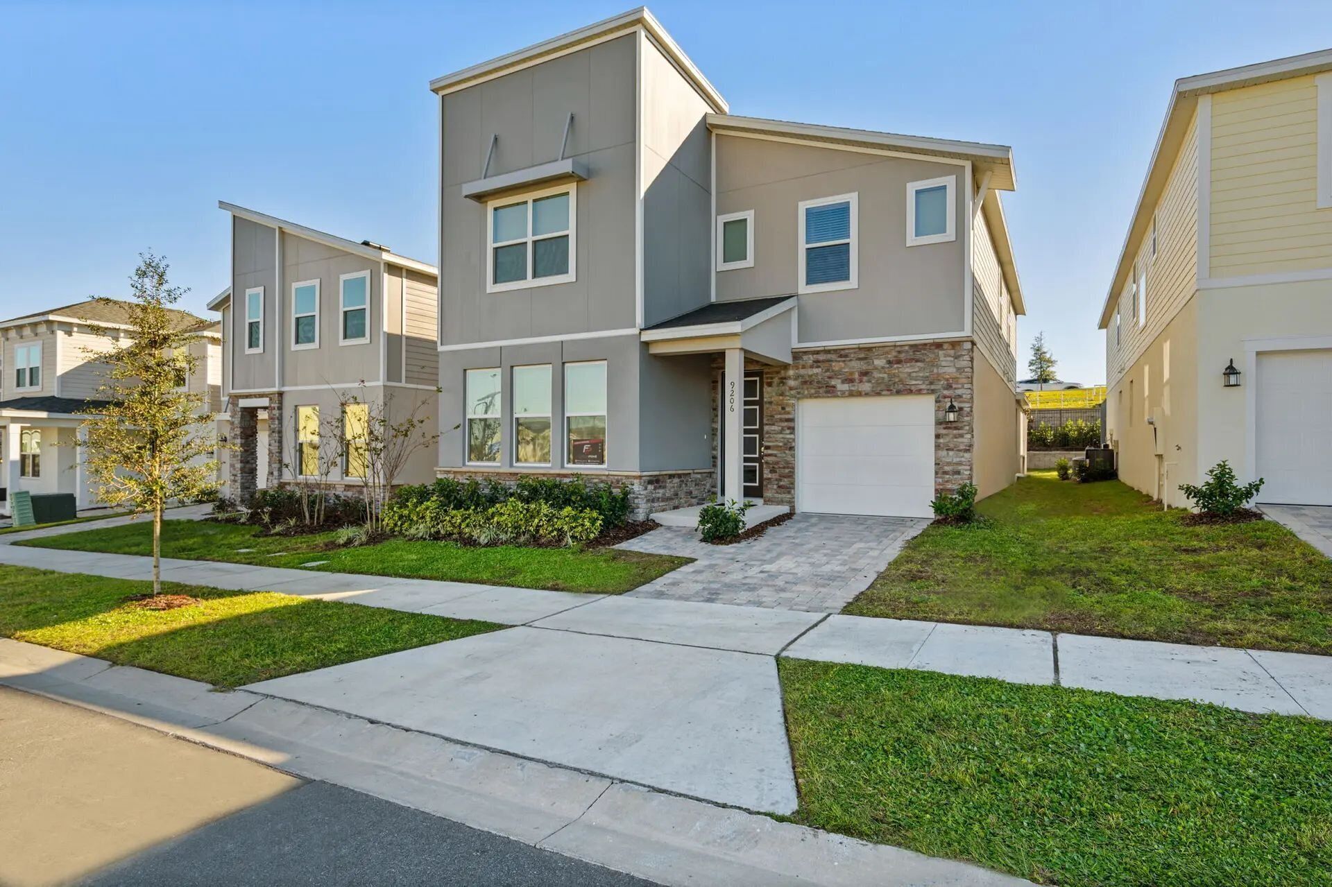 A modern two-story residential building with a stone facade, a front porch, and a garage.