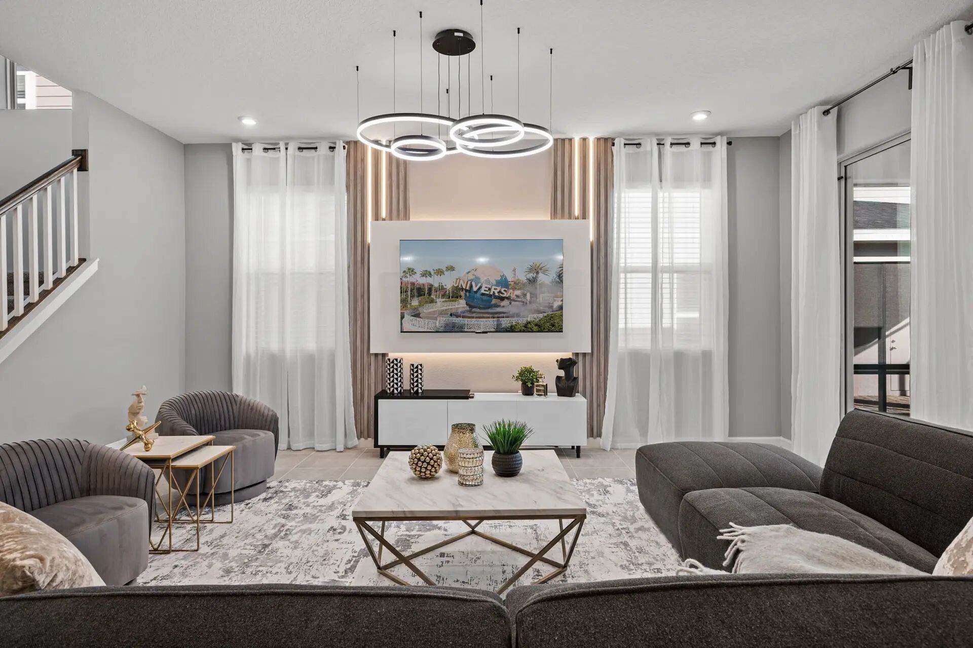 A modern living room with a flat-screen TV mounted on the wall, a coffee table, sofas, and a staircase.