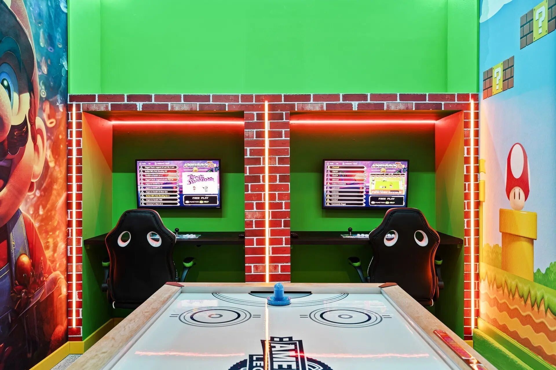 Une pièce équipée de deux postes de jeu, chacun doté d’un écran affichant un menu de jeu, et d’une table ornée d’un logo au centre.