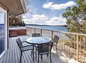 Een terras met een glazen tafel en stoelen, een jacuzzi en uitzicht op een meer.