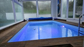 Une piscine intérieure avec des parois en verre transparent, une terrasse en bois et un escalier pour accéder à la piscine.
