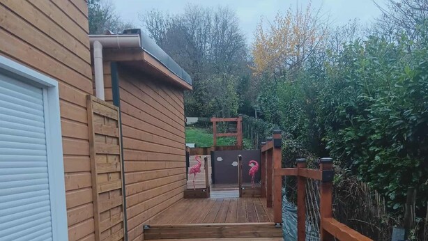 Une terrasse en bois qui mène à un espace clos offrant une vue sur un jardin et des arbres.
