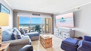 Una sala de estar con televisor, sofá, un cofre de madera y vista a la playa.