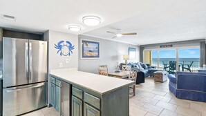 Una cocina moderna con un refrigerador de acero inoxidable, un comedor con mesa y sillas, y una sala de estar con un sofá azul.