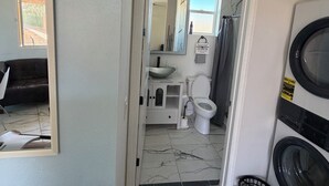 Et badeværelse med toilet, vask og spejl. Der er en vaskemaskine og en kurv på gulvet.
