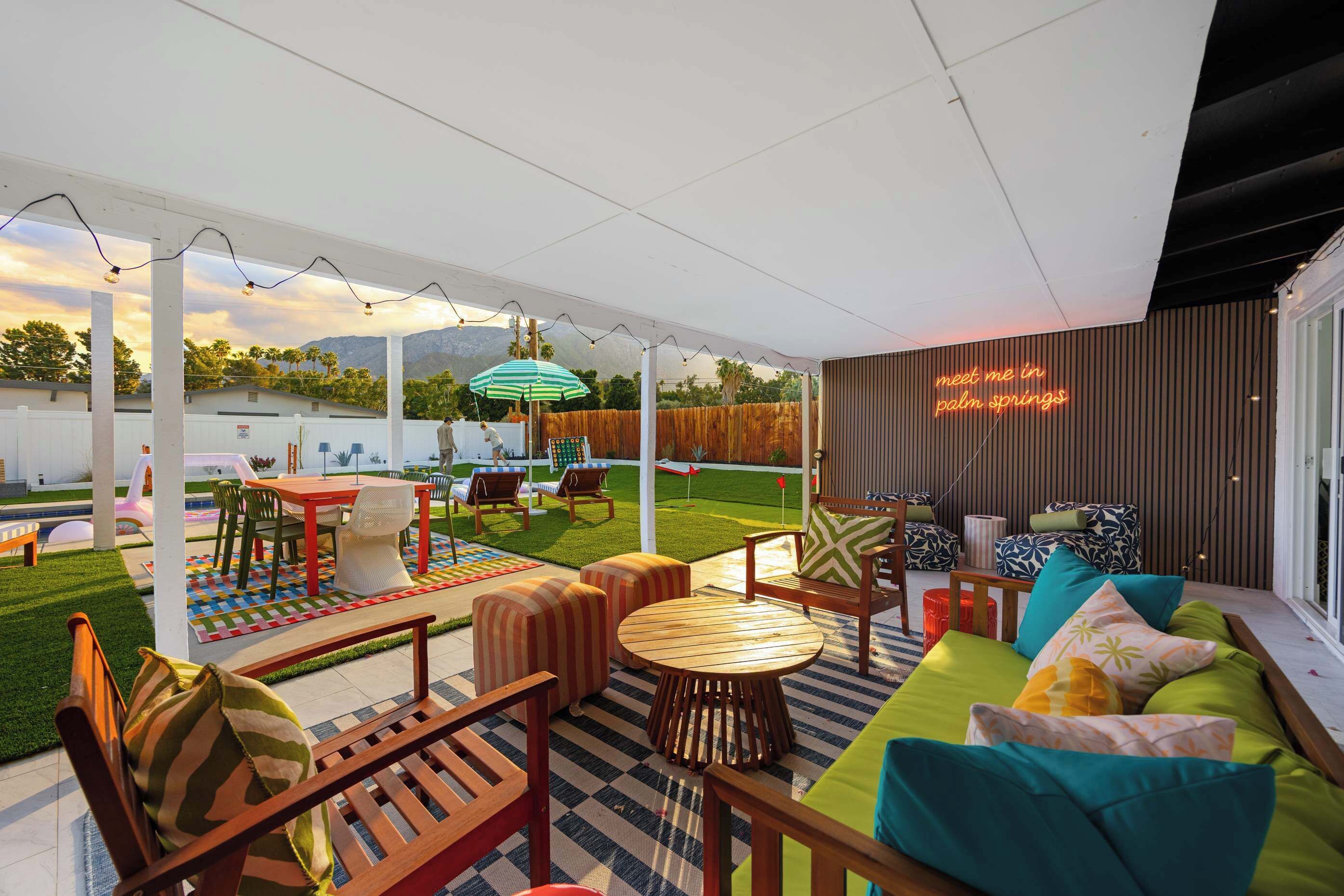 Eine überdachte Terrasse im Freien mit Sitzgelegenheiten, einem Tisch und einem Neonzeichen.