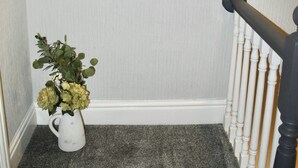Un corridoio con una parete bianca, tre specchi circolari e un vaso bianco con fiori.