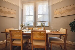 Ruokailuhuoneessa on puinen pöytä, johon on katettu neljälle, ja pöydän ympärillä on rottinkituoleja, joissa on pehmusteet.