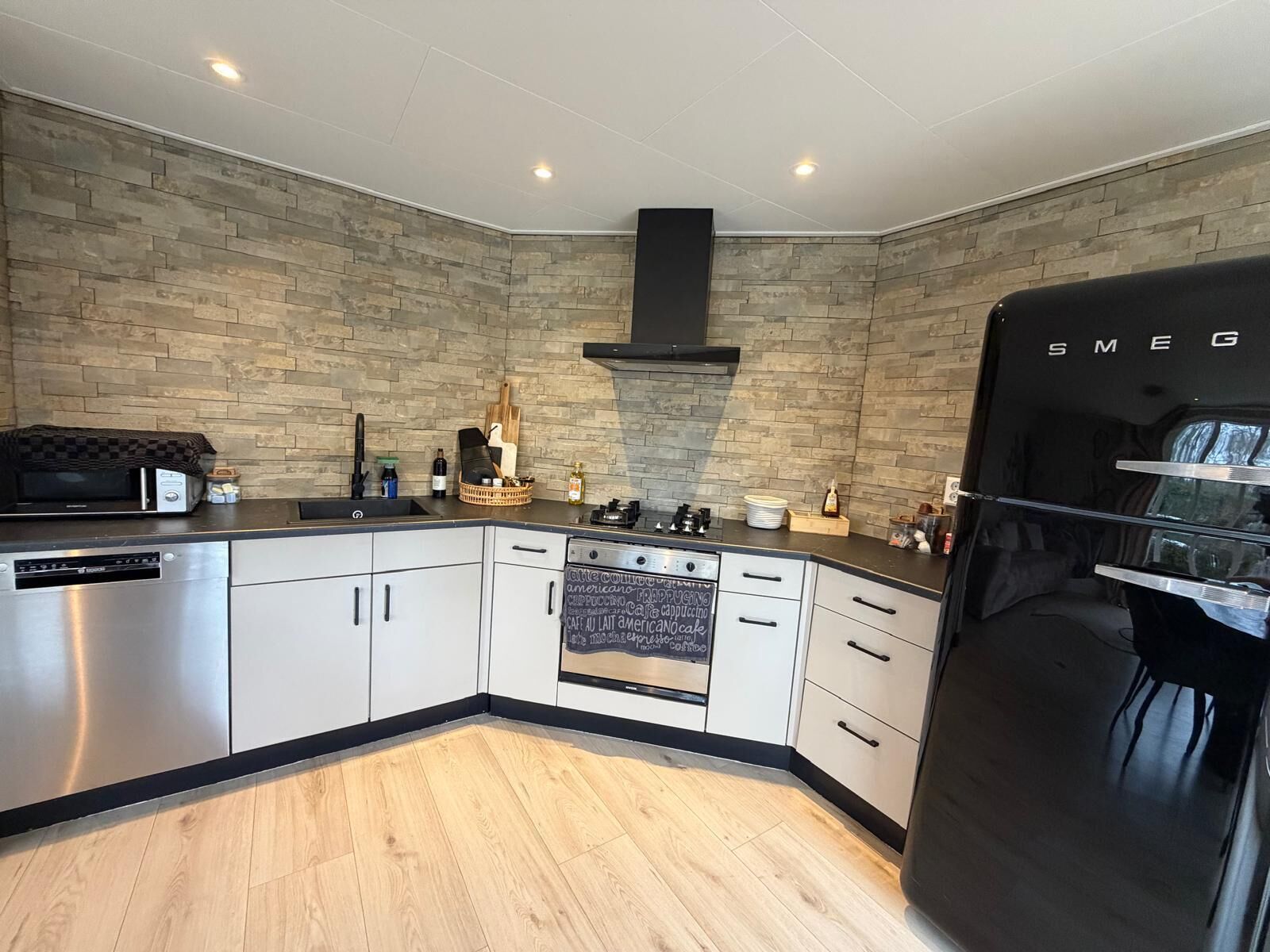 A modern kitchen with a stone backsplash, a black refrigerator, and a built-in oven.