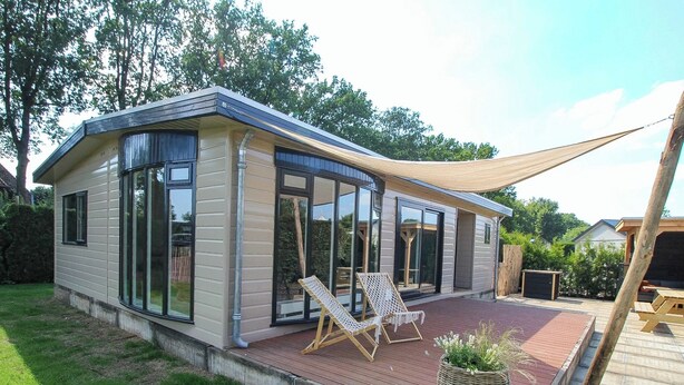 A modern house with large windows, a deck, and two lounge chairs. - VELUWE WELLNESS CHALET - Private Hot Tub and Sauna on Park with Swimming Pool (Voorthuizen)