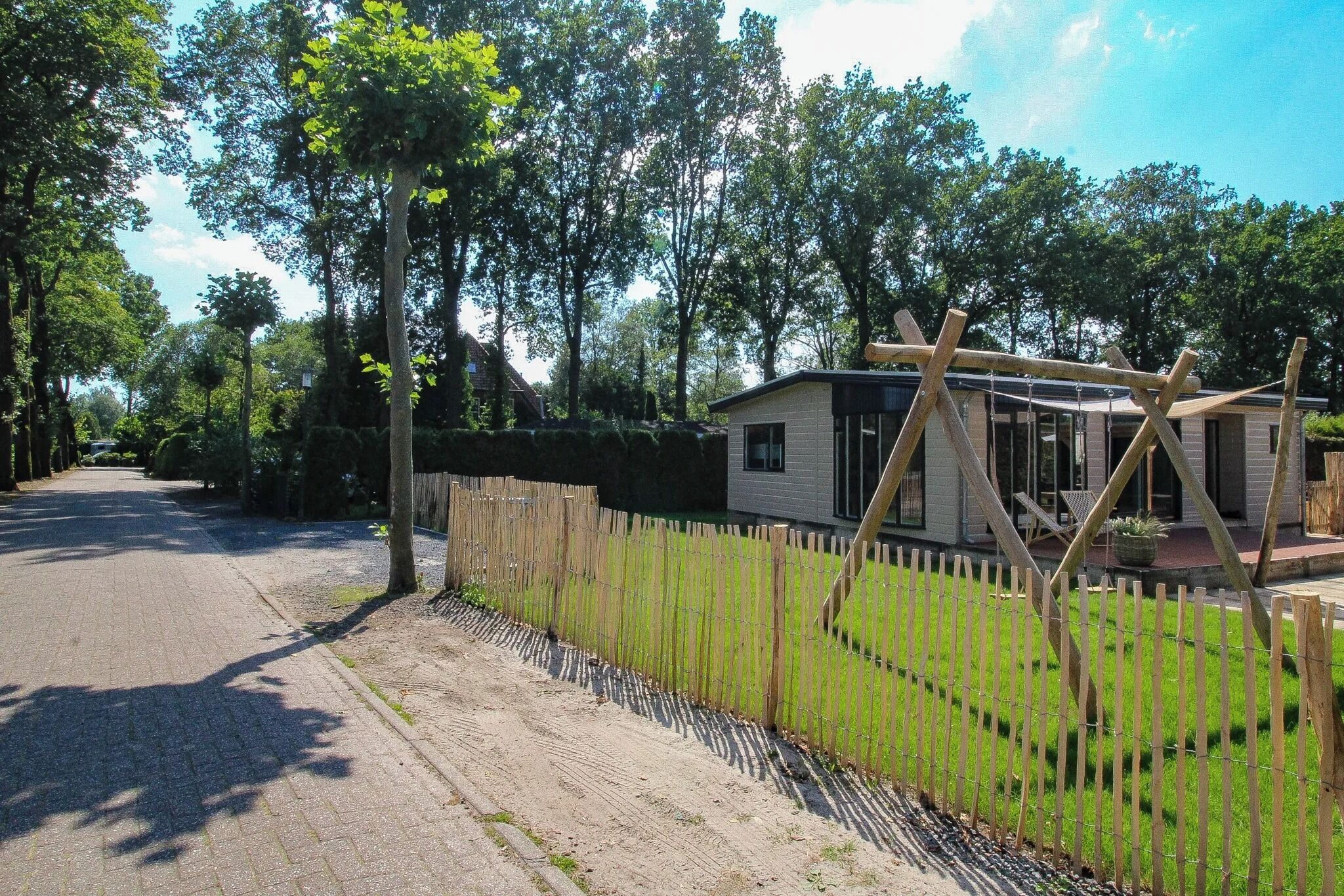 Una calle residencial con una casa, un cerco de madera y un cielo despejado.
