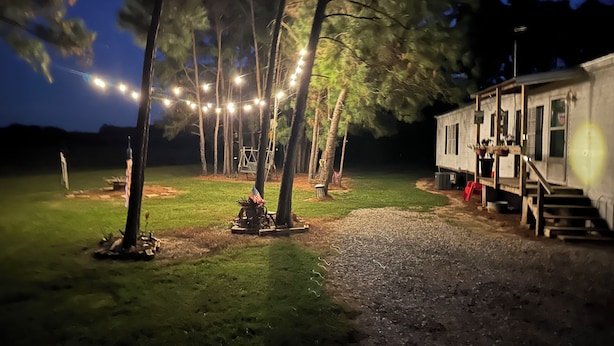 Eine rustikale Holzhütte mit einem Kiesweg, umgeben von Bäumen und Lichterketten.