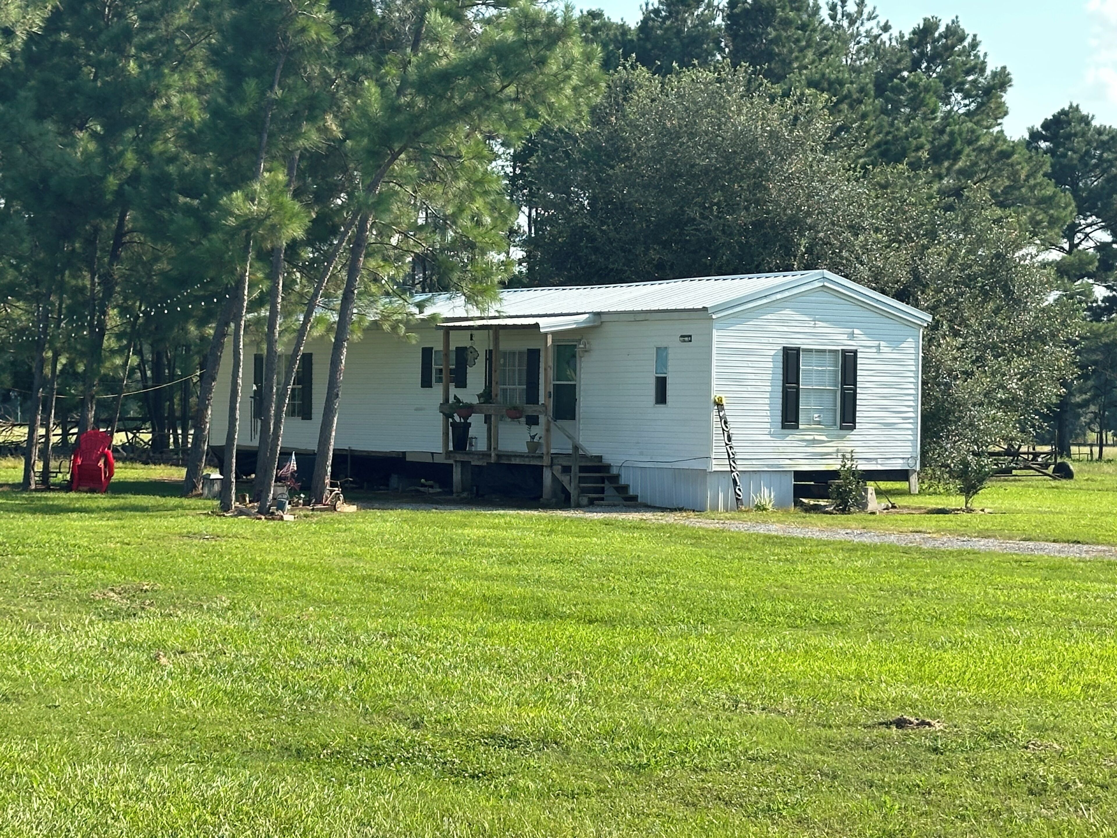 A single-story house with a porch, surrounded by a grassy field and trees.