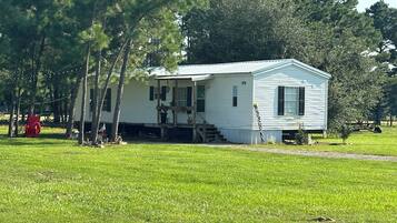 A single-story house with a porch, surrounded by a grassy field and trees.