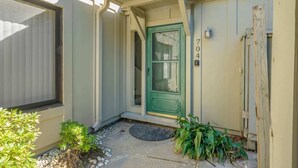 Una casa con puerta verde, buzón y pequeño jardín con plantas y felpudo.
