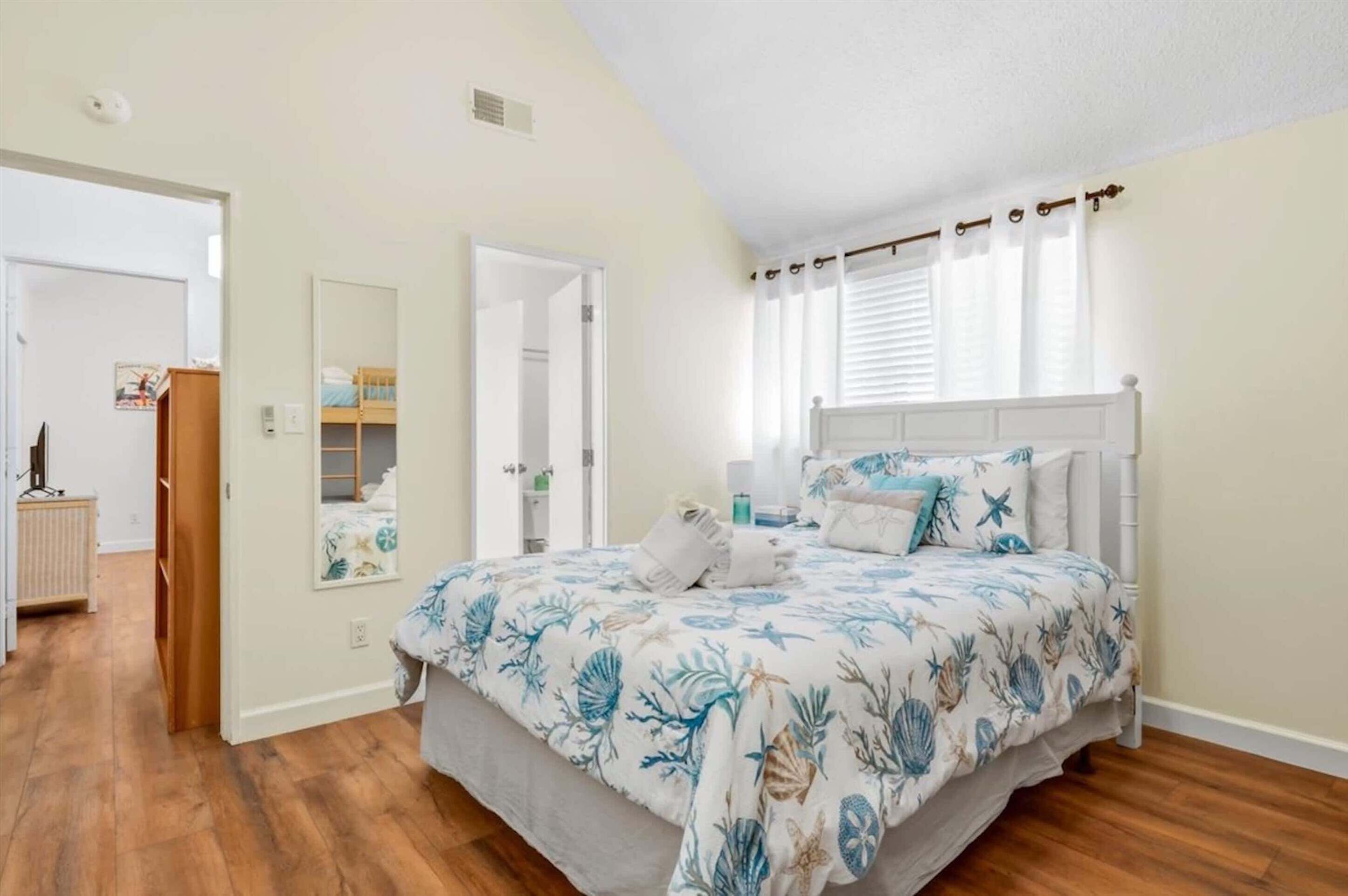 Een slaapkamer met een bed, een spiegel en een raam met gordijnen.