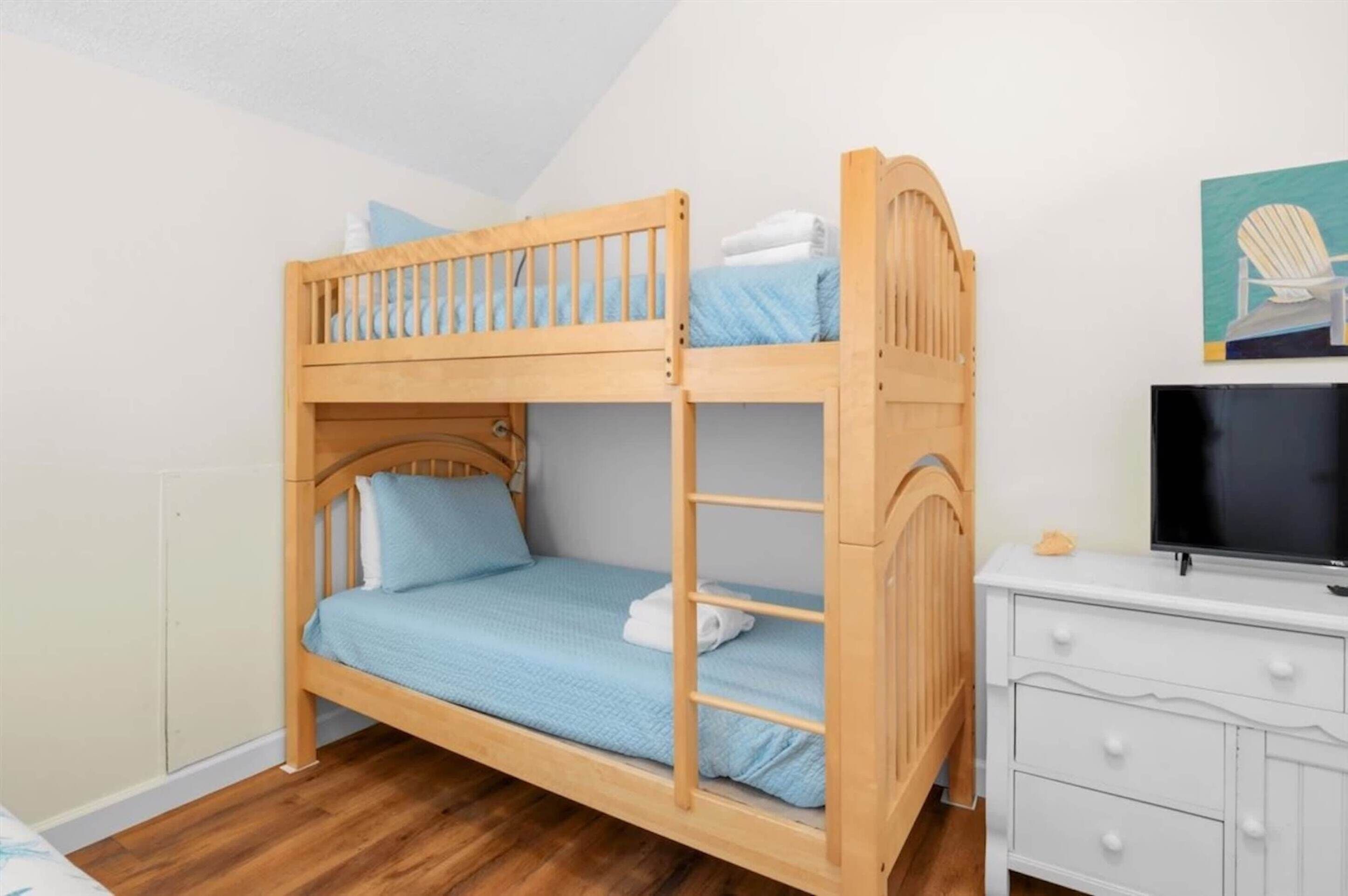 A bunk bed with a wooden frame, a television on a white dresser, and a painting on the wall.