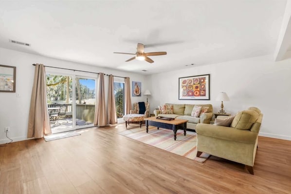 A spacious living room with a sliding glass door leading to a patio, a ceiling fan, and a large abstract painting on the wall.