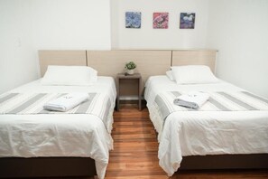 A hotel room with two single beds, a wooden headboard, a small bedside table with a plant, and three framed floral artworks on the wall. - Hotel Quinta Del Café (Fredonia)