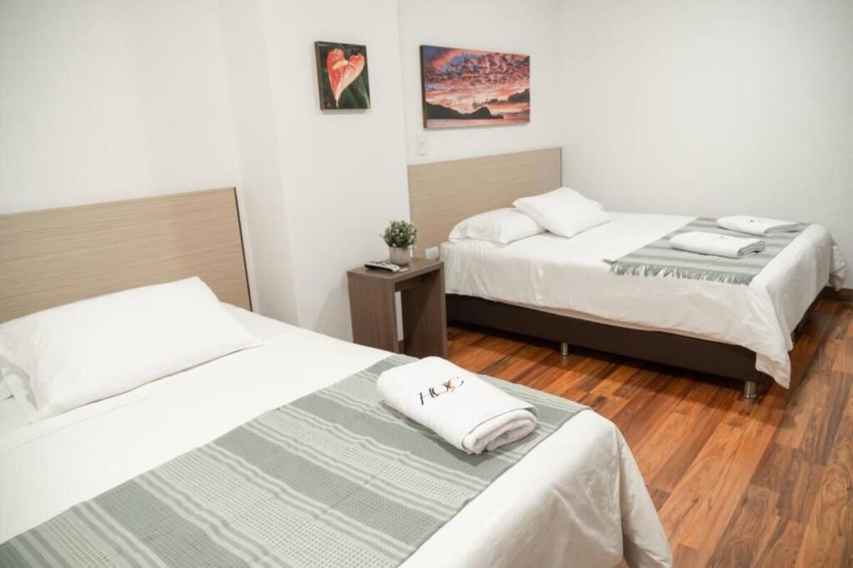 A hotel room with two beds, a nightstand, a small table, and a wall-mounted painting.