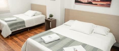 A hotel room with two single beds, a wooden floor, a painting of a sunset, and a small plant on a nightstand.