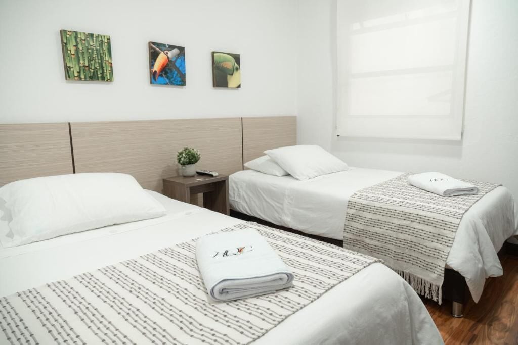 A hotel room with two beds, a nightstand with a plant, and artwork on the wall.