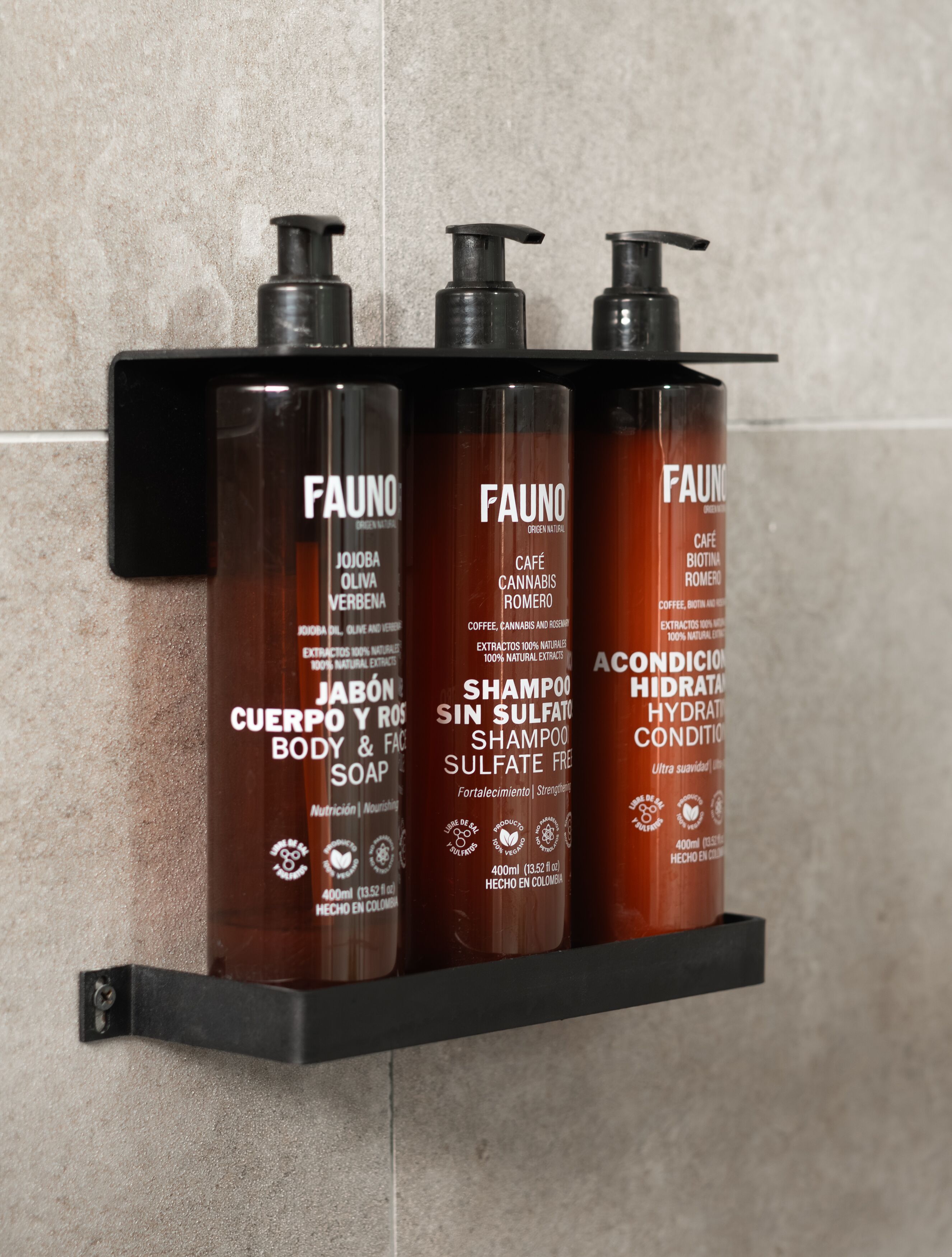 Three bottles of Fauno shampoo and conditioner on a black shelf against a tiled wall.