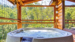 Ein Whirlpool in einer Holzhütte mit großen Fenstern mit Blick auf einen Wald.