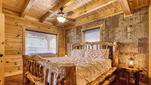 Ein rustikales Schlafzimmer mit Holzboden, einem Bett, zwei Fenstern, einem Deckenventilator und einem Nachttisch mit einer Laterne.