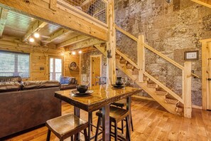 A rustic interior with a wooden staircase, a dining table with stools, a leather sofa, and a fireplace. - Log Cabin - Hot Tub, W/D, Grill, Pets Free in charming Gatlinburg (Gatlinburg)