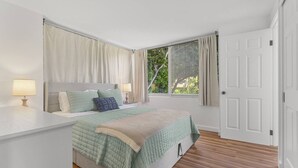 Quarto com cama, mesas de cabeceira, janela com cortinas e porta.