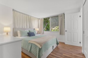 Un dormitorio con cama, mesitas de noche, una ventana con cortinas y una puerta.