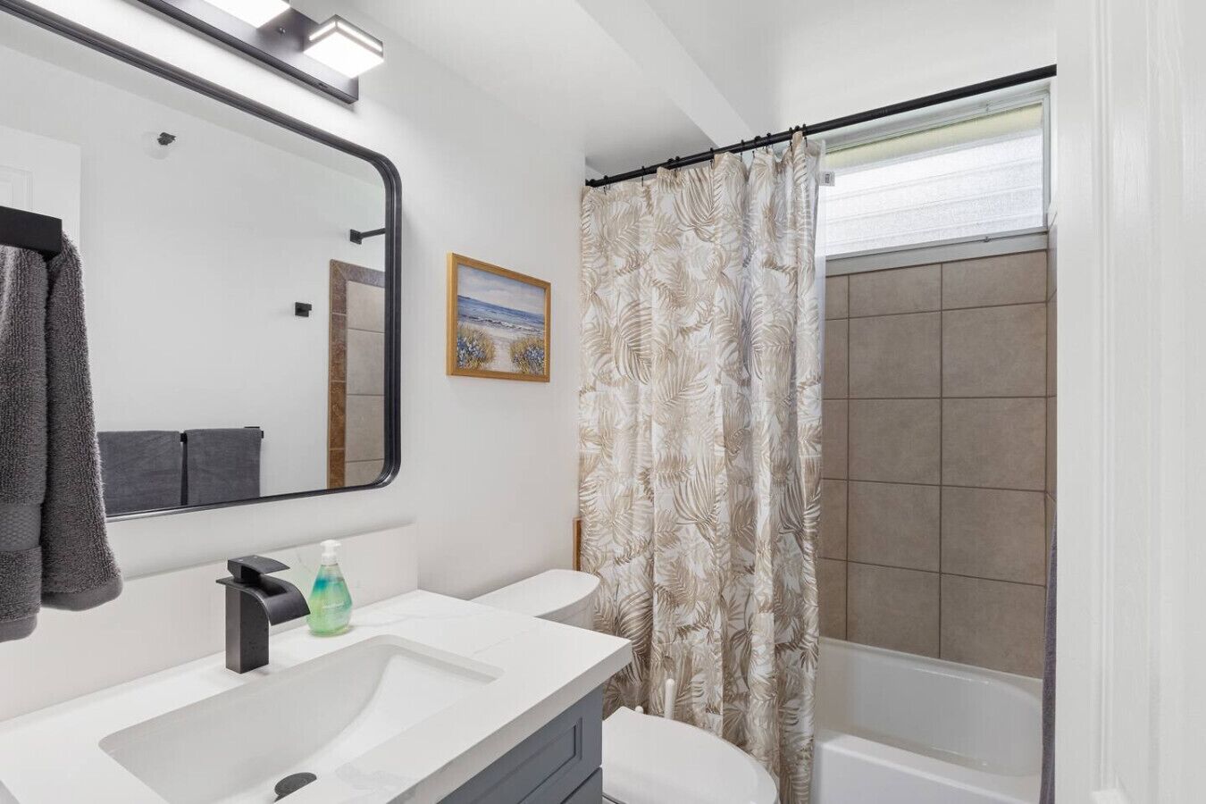 Une salle de bain moderne avec un grand miroir, deux lavabos, des toilettes et une douche dotée d’un rideau à motifs.