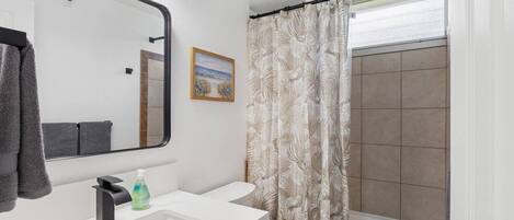 Une salle de bain moderne avec un grand miroir, deux lavabos, des toilettes et une douche dotée d’un rideau à motifs.