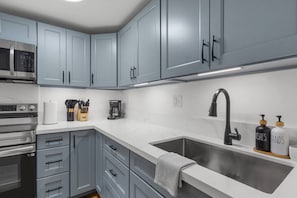 Una cocina moderna con armarios grises, electrodomésticos de acero inoxidable y un lavamanos grande.