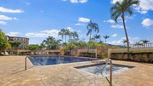 Área de piscina com piso de pedra, palmeiras e uma grade.