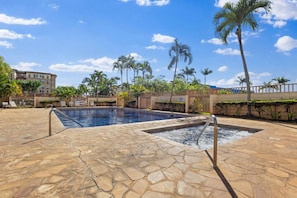 Zona de piscina con suelo de piedra, palmeras y una valla.