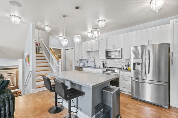 A modern kitchen with white cabinets, stainless steel appliances, and a central island with bar stools. - Modern Island Living | Parking, AC, Fast WiFi, W/D (Ewa Beach)