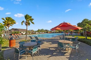 A poolside area with lounge chairs, a table, and a red umbrella. - Modern Island Living | Parking, AC, Fast WiFi, W/D (Ewa Beach)