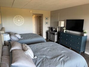 Quarto de hotel com duas camas, uma cômoda, uma televisão e uma cafeteira.