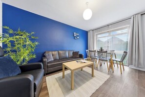 Un salon moderne avec un mur d’accent bleu, un canapé en cuir, une table basse en bois et un coin repas avec des chaises jaunes.