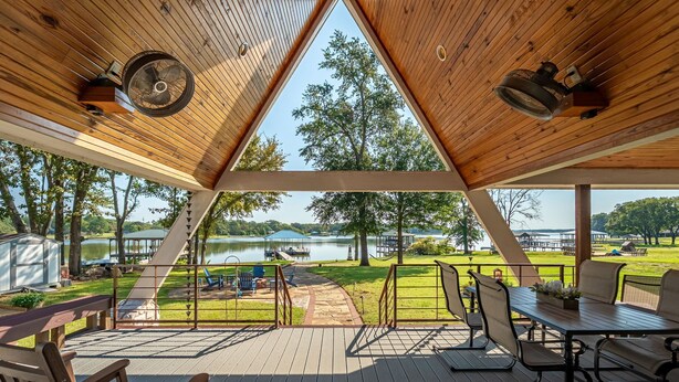 Um deck de madeira com vista para um lago, mesas de piquenique e um gazebo.