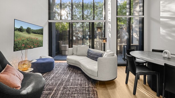 A modern living room with a curved sofa, a flat-screen TV, and a dining area with a table and chairs. - Bright Inner-north Stay With Pool Access (Melbourne)